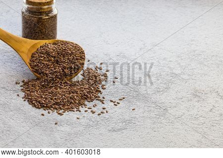 Flax Seeds In A Wooden Spoon And A Glass Jar On Concrete Background, A Dietary Product That Reduces