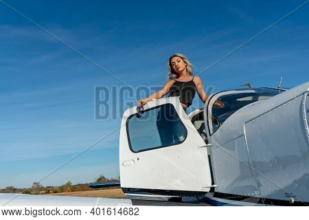 A gorgeous young blonde model poses outdoors with a single engine aircraft at a local airport
