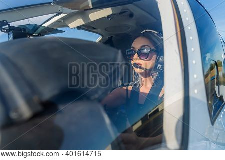 A gorgeous young blonde model poses outdoors with a single engine aircraft at a local airport