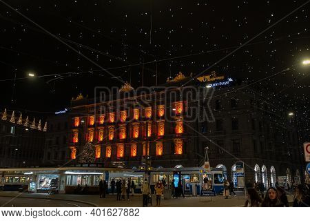 Paradeplatz At Christmastime At Night. Illuminated Windows Of Headquarter Of Banks And Tram Station 