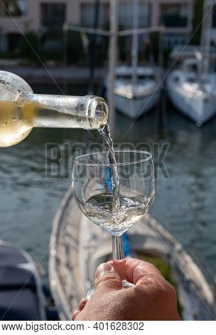 Pouring Of Cold White Wine In Glass In Summer With Sail Boats Haven Of Port Grimaud On Background, P