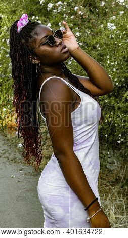 Vertical Shot Of A Young African Woman Dressed In A White Dress And Sunglasses Poses Next To Some Sm