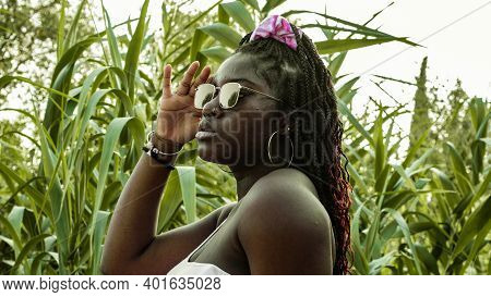 The Young African Woman Puts On Her Sunglasses.the Plants Brings The Scene To Life.
