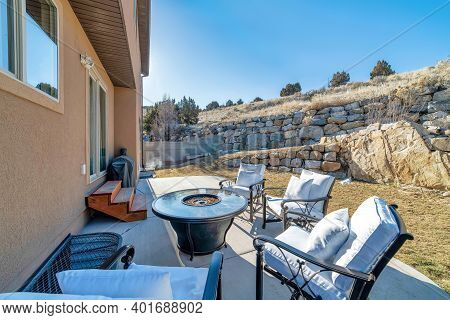 Fire Pit And Paved Patio At Sunny Backyard Of House With Stone Retaining Wall