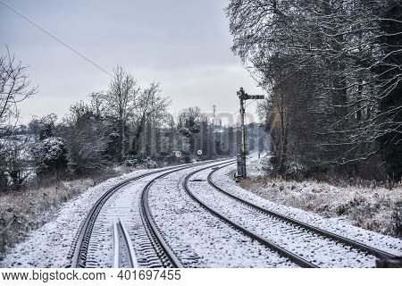 Railway Line Bending To The Right In The Snow With Signal To The Right Of The Line In The English Co