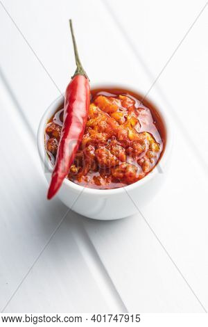 Red hot chili paste and chili pepper on white table.
