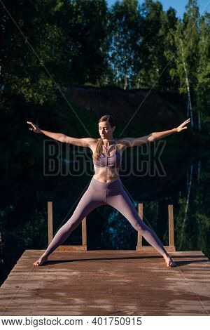 Young Woman Relaxing By The Lake At Sunset, Harms Outstretched. Doing Youga In The Morning At Forest