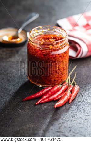 Red hot chili paste and chili pepper in jar on black table.