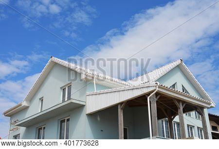 A Light Blue House With Stucco Walls, White Cross Gabled Metal Roof, Rain Gutter System, And A Cover