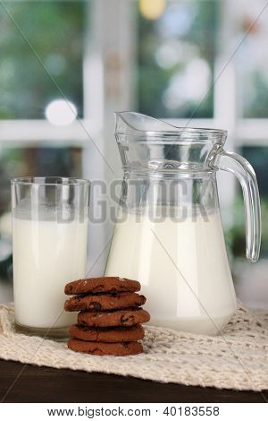 Jarra e copo de leite com biscoitos em malhas de gola alta na mesa de madeira no fundo da janela