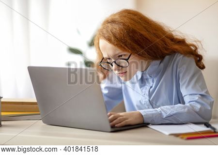 Technology And Youth Concept. Portrait Of Focused Schoolgirl Using Computer, Sitting At Table Too Cl