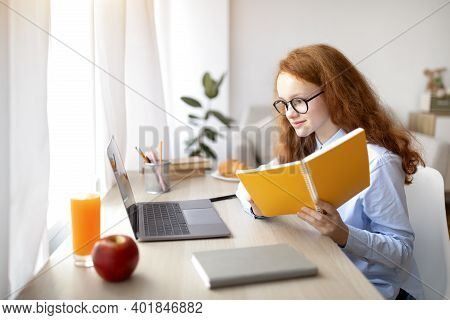 Doing Homework. Portrait Of Pretty Young Teenage Schoolgirl Wearing Glasses, Holding Notebook And Us