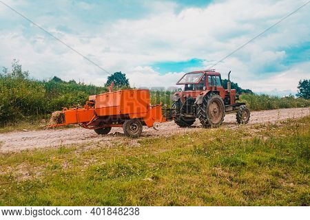 The Process Of Harvesting Hay For Cattle, A Tractor Making Bales In The Field, Old Machinery.