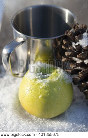Green Apple In The Snow With A Cedar Cone And A Metal Mug For A Hot Drink. Winter Set For A Snack In