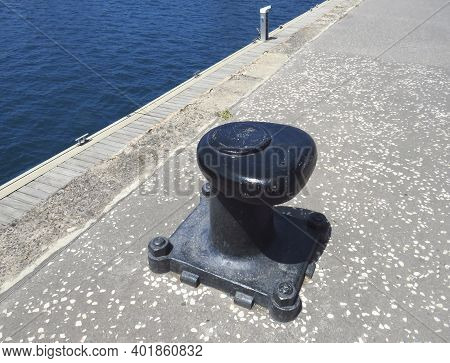 Black Metal Mooring Bollard In Marina And Port Terminal. Close Up Of Mooring Noray On A Dock. Port C