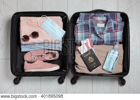 Open Suitcase With Passport, Tickets, Sanitizer And Protective Mask On Wooden Floor, Top View. Trave