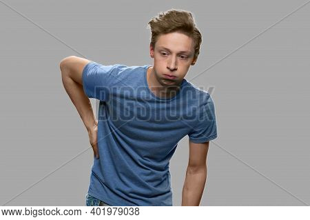 Teen Boy With Back Ache On Gray Background. Unhappy Teen Guy Suffering From Back Ache. Health Probel