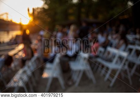 People Are Watching A Concert Of Classical Music. Blurred Young And Adult Women And Men And Other Pe