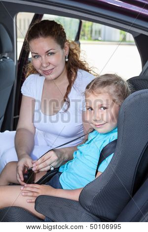 Small Child In Car Safty Seat With Helping Mother. Caucasian Family