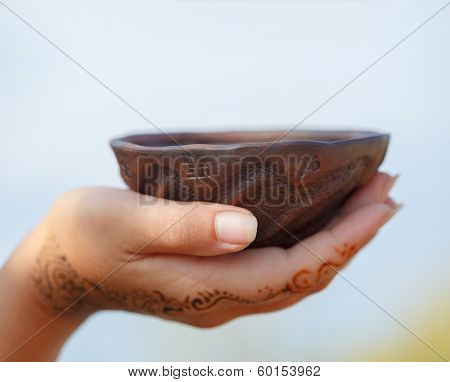 Female hand with traditional Indian wedding henna mehendi pattern holding a clay cup with widespread ethnic symbols.