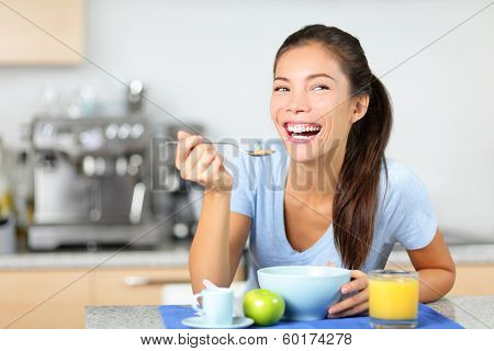 Woman eating breakfast cereals at morning table smiling happy and morning fresh. Beautiful young multiracial woman sitting in her kitchen at home. Mixed race Asian Caucasian female model.