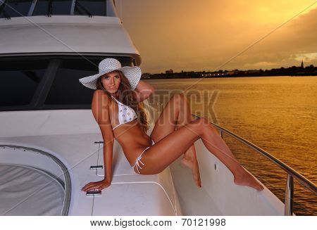 Swimsuit model wearing white bikini and hat posing on deck of luxury yacht