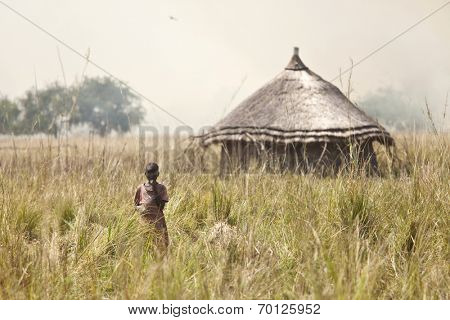LILIIR, SOUTH SUDAN-DECEMBER 4 2010, Unidentified child stands in field with grassfires in the background in the village of Liliir, South Sudan.