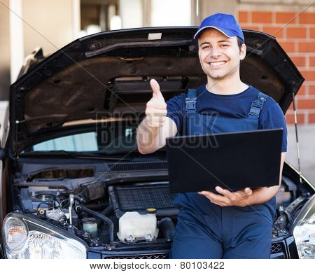 Happy mechanic using a laptop computer to check a car engine