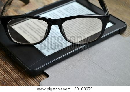 Black ereader with retro glasses on wooden table