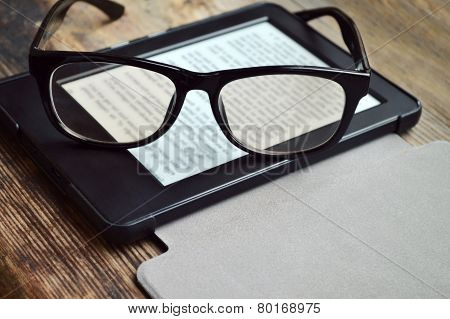 Black ereader with retro glasses on wooden table