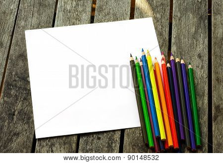 Colored pencils with paper on wooden desk