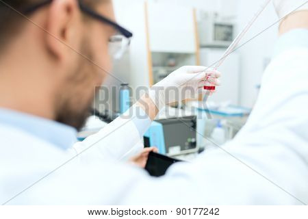 science, chemistry, biology, medicine and people concept - close up of male scientist with test tube and pipette making research in clinical laboratory
