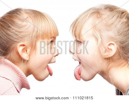 Two little girls stick out tongues teasing each other