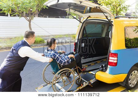 Driver Helping Man On Wheelchair Getting Into Taxi