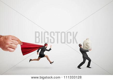 big mans hand holding the red cloak of superwoman that chasing the thief with big bag of money over light grey background