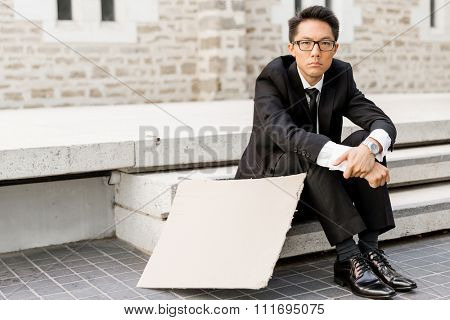 Businessman in a city street hsitting next to blank banner