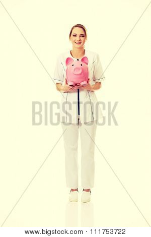 Young beautiful female doctor holding a piggybank.