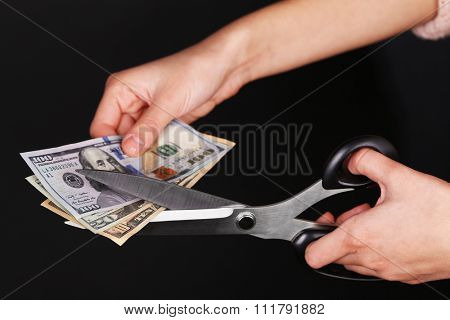 Hands with scissors cutting dollar banknotes, on black background