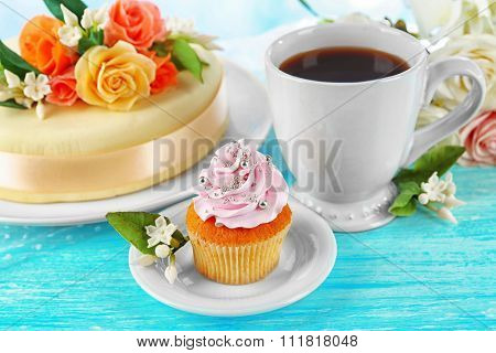 Cake with sugar paste flowers and cupcake, on light background