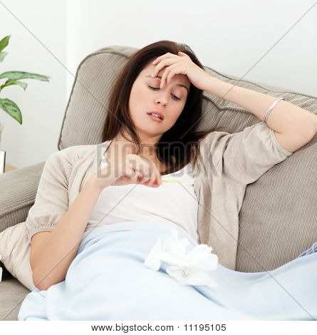 ソファの上に休んでいる間で温度計を見て病気の女性