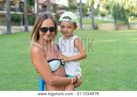Young mother and smiling baby boy son in green baseball cap playing in the sea in the day time. Positive human emotions feelings joy. Spring and summer holidays.;