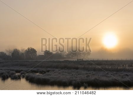 Winter landscape near Giethoorn in Overijssel with frozen grass old farm and fog in the morning light Netherlands.