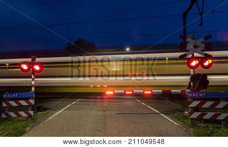 Woudenberg Netherlands - August 21 2017: Yellow and blue NS train with lights passing a railway crossing in the night in the Netherlands.