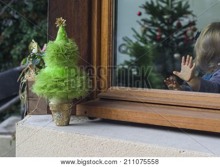 Little girl with a palm on the glass looking at the Christmas tree