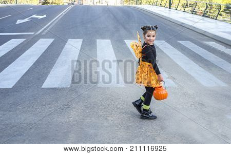 Little girl at zebra crossing in halloween costumes. She is walking towards children party site. Badajoz Spain