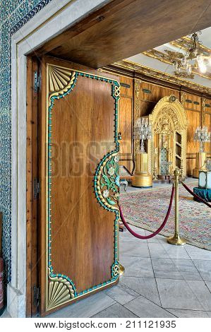 Cairo Egypt - October 21 2017: Wooden floral pattern ornate door revealing residence of prince's mother with golden ornate niche wooden wall and marble tiled floor covered with carpets at Manial Palace of Prince Mohammed Ali Tewfik