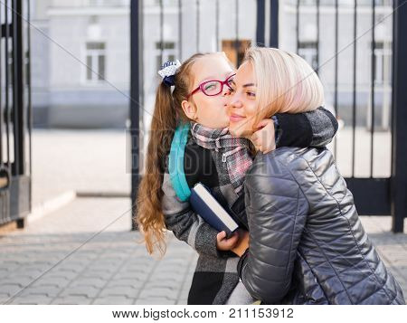 A girl goes to school with a briefcase and a book kisses good-bye to her mother