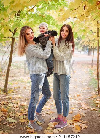 Mom and her son in the autumn in the park holding him in his arms with a girlfriend