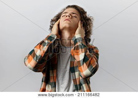 Studio shot of irritated student in plaid shirt throwing back head closing eyes and massaging his temples feeling stressed facing deadline while working on his diploma project late at night