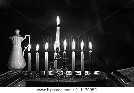 Burning Chanukah. The lit Chanukiah. Jewish holiday Hanukkah. Black and white photo. Porcelain jug with oil